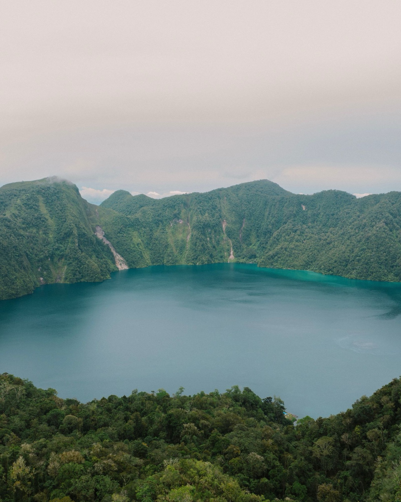 Aerial view of a deep blue crater lake ringed by green mountains