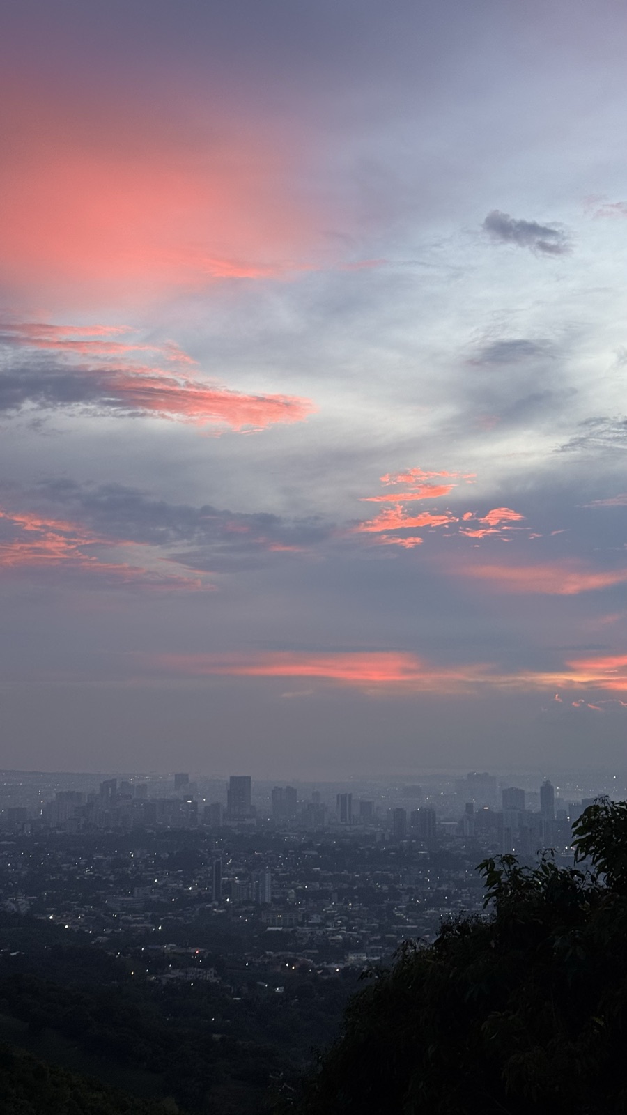Pink and purple clouds at dusk above a hazy city skyline