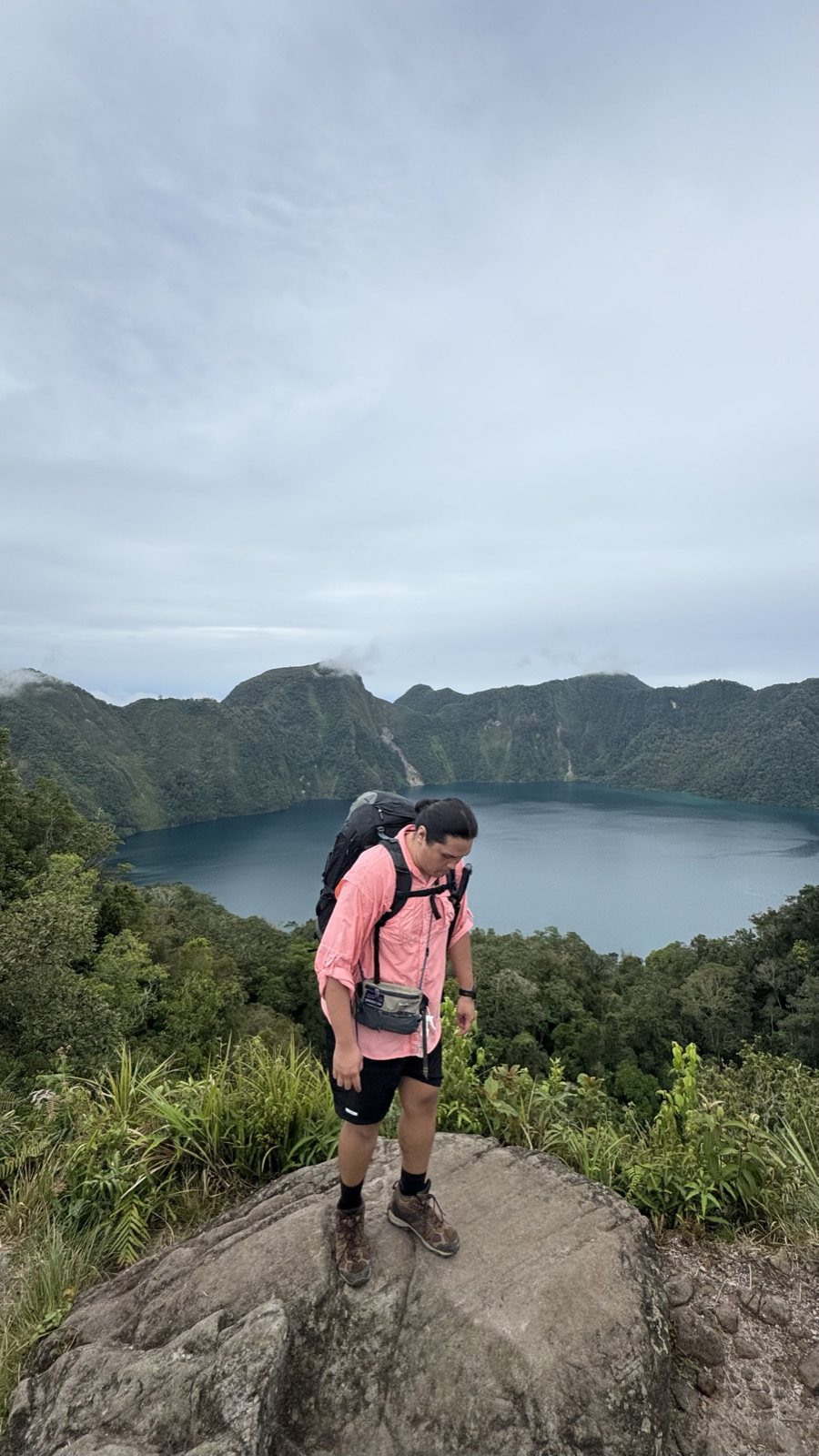 Hiker with a backpack standing on a boulder above a mountain lake